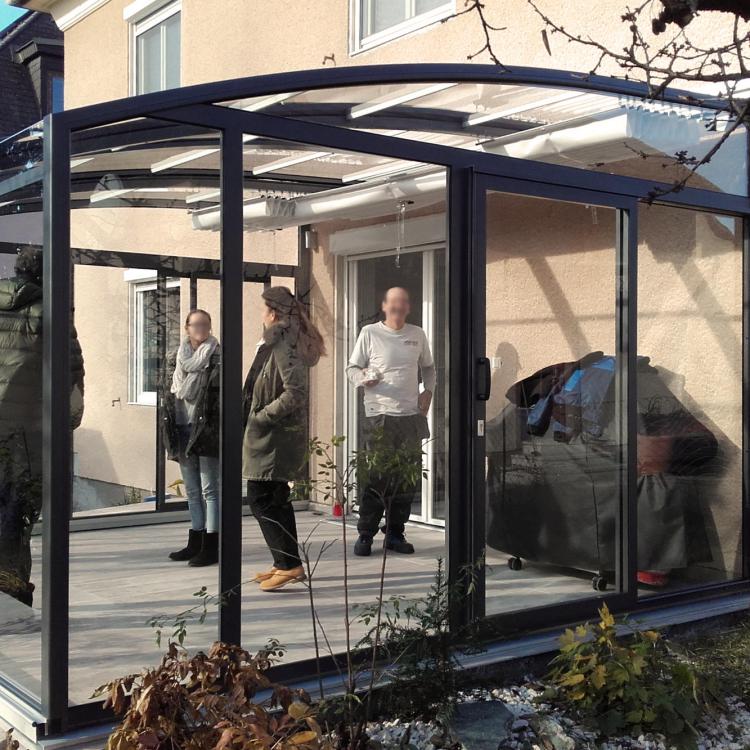 Abri de terrasse Topaz coulissant transparent implanté en ville devant le fenêtre du salon
										